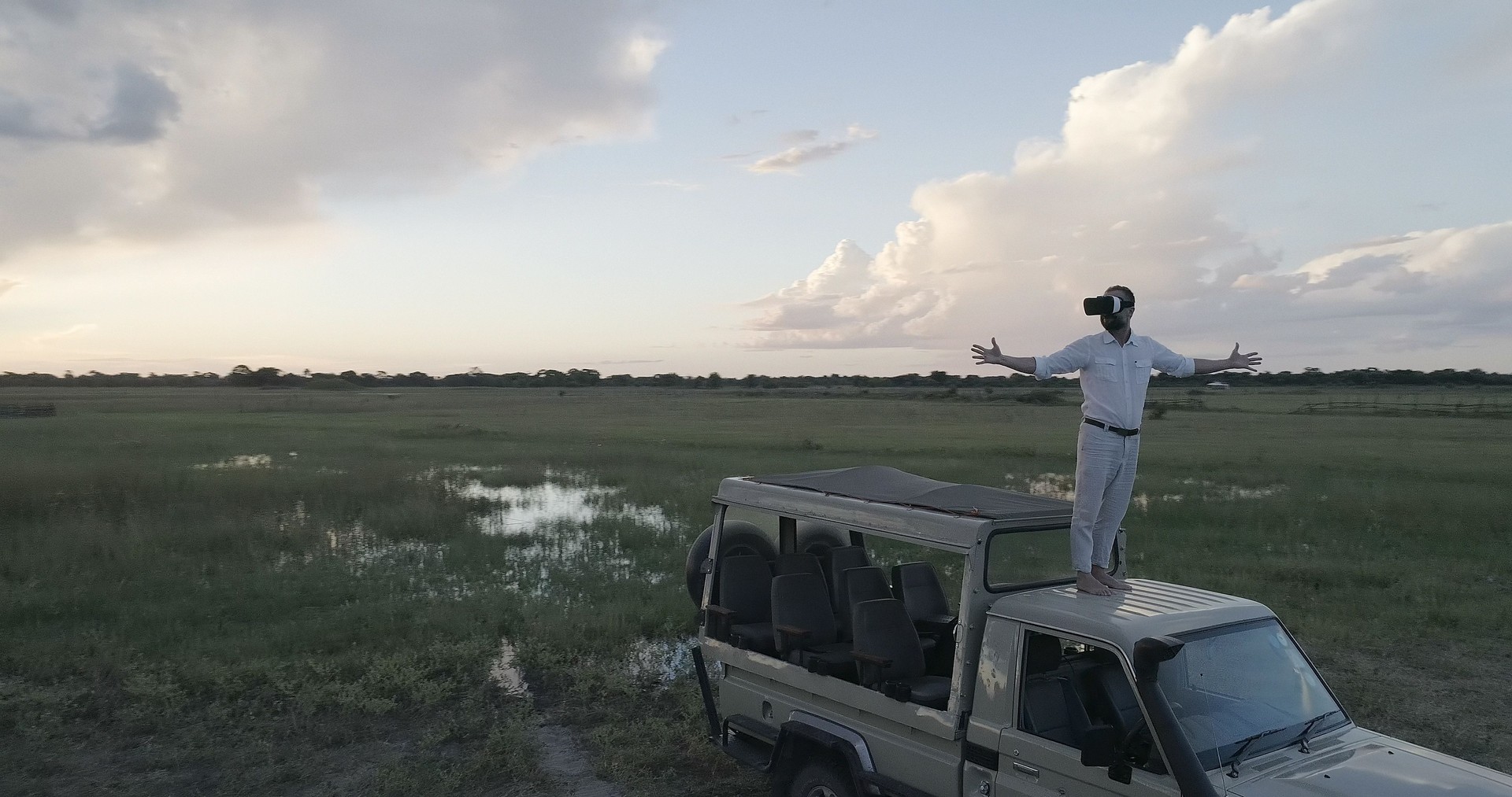 Virtual safari. Man standing on a off-road vehicle, admiring savannah with virtual reality set